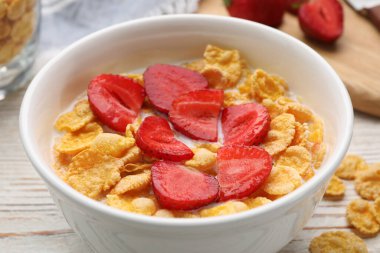 Bowl of tasty crispy corn flakes with milk and strawberries on white wooden table, closeup