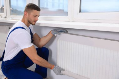 Professional plumber installing new heating radiator in room