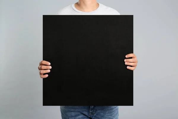 Man holding black blank poster on grey background, closeup. Mockup for design