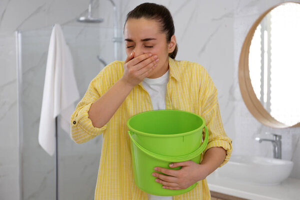 Young woman with bucket suffering from nausea in bathroom. Food poisoning