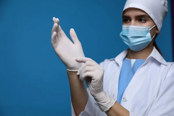 Dokter Beschermend Masker Zet Medische Handschoenen Tegen Blauwe Achtergrond — Stockfoto