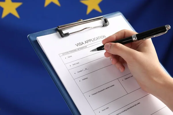 Woman filling visa application form against flag of European Union, closeup