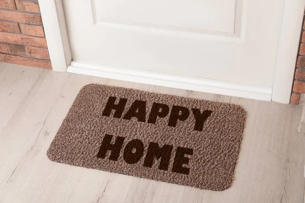 Door mat with words Happy Home on wooden floor in hall, above view