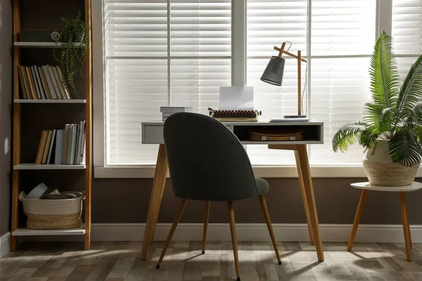 Comfortable writer's workplace interior with typewriter on desk in front of window