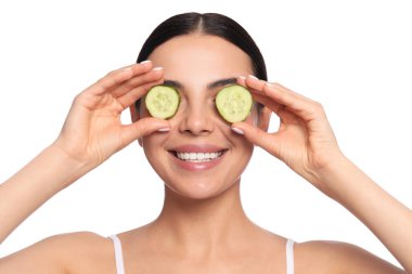 Beautiful young woman putting slices of cucumber on eyes against white background