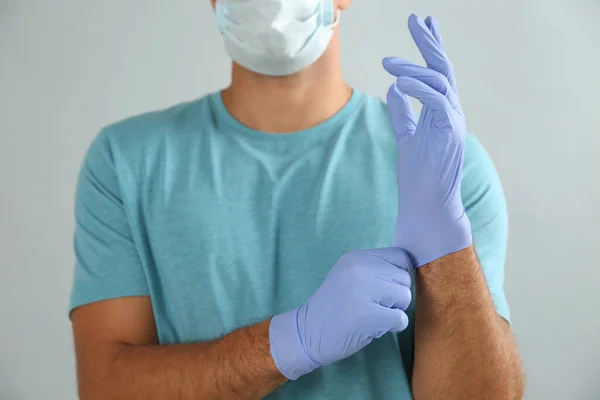Man Protective Face Mask Putting Medical Gloves Grey Background Closeup — Foto Stock