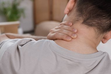 Man suffering from neck pain indoors, back view