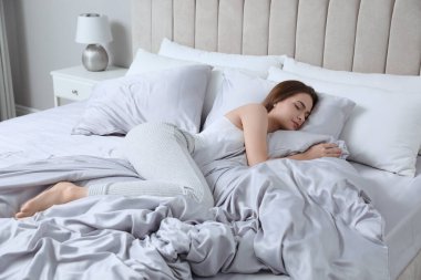 İpek çarşaflarla rahat bir yatakta uyuyan genç bir kadın.