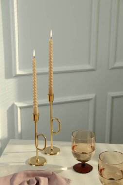 Glasses of wine near burning candles on white table indoors