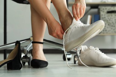 Rahatsız ayakkabılarını çıkaran ve ofiste spor ayakkabılarını giyen bir kadın.