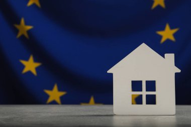 House model on light grey table against flag of European Union. Space for text