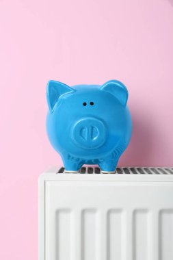 Piggy bank on heating radiator against pink background