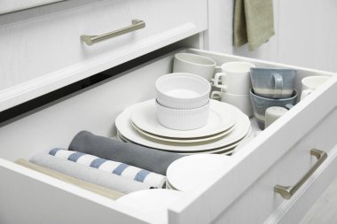 Open drawer of kitchen cabinet with different dishware and towels, closeup
