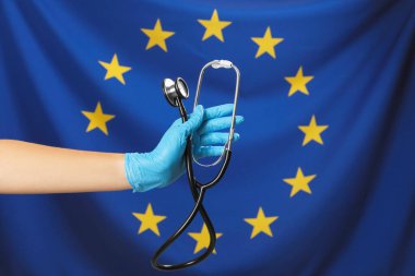 Woman holding stethoscope against flag of European Union, closeup