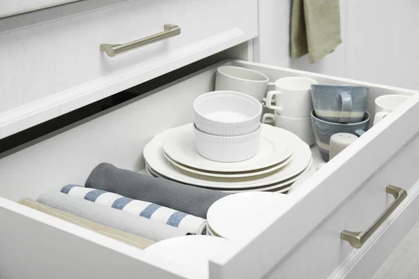 Open drawer of kitchen cabinet with different dishware and towels, closeup