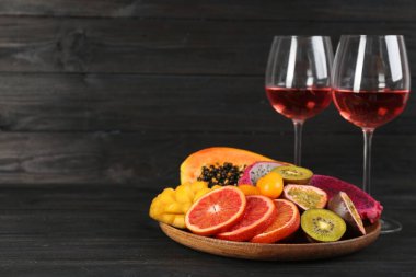 Delicious exotic fruits and wine on black wooden table. Space for text