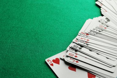 Deck of playing cards on green table, closeup. Space for text