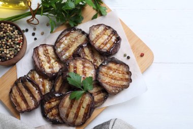 Delicious grilled eggplant slices with parsley and spices on white wooden table, flat lay