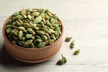 Bowl of dry cardamom pods on white wooden table, closeup. Space for text