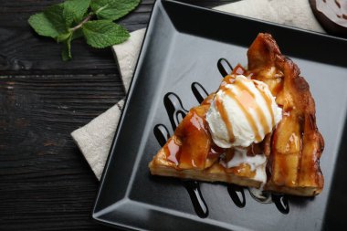 Slice of traditional apple pie with ice cream on black wooden table, flat lay