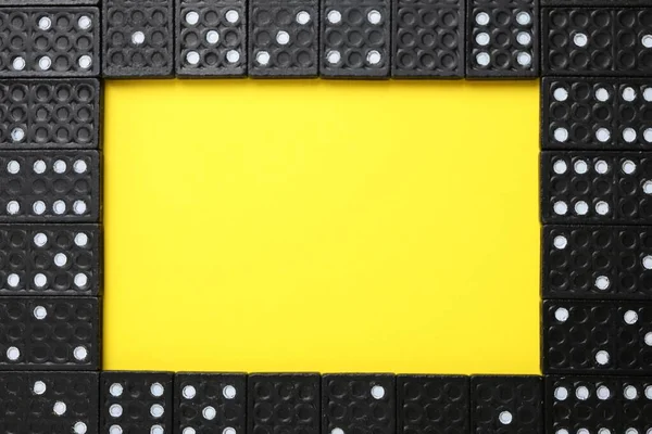 Frame of black domino tiles on yellow background, flat lay. Space for text