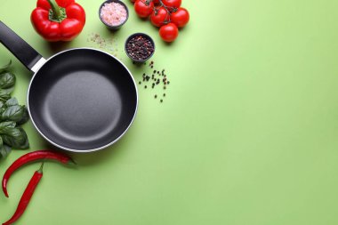 Flat lay composition with frying pan and fresh products on green background, space for text