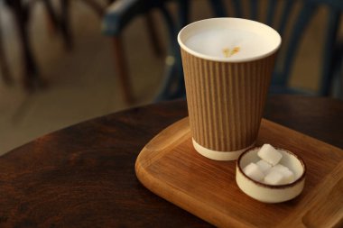 Delicious coffee in cardboard takeaway cup and bowl of sugar cubes on wooden table indoors, space for text