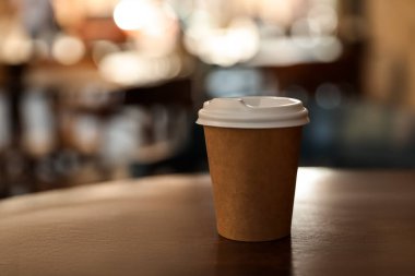Cardboard takeaway coffee cup with plastic lid on table in outdoor cafe, space for text