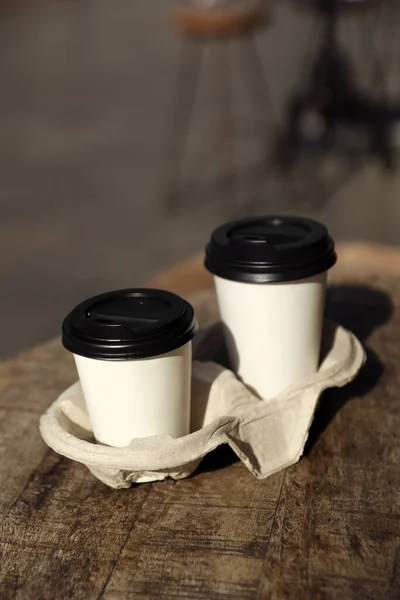 Cardboard takeaway coffee cups with plastic lids and holder on wooden table in city