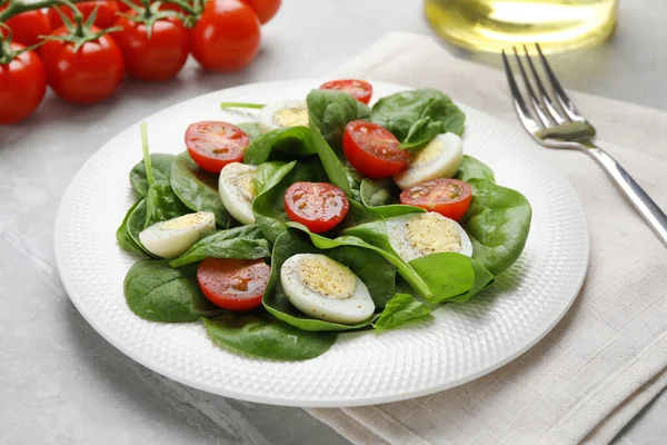 Delicious salad with boiled eggs, tomatoes and spinach on light grey table, closeup
