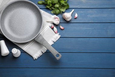 Empty frying pan, garlic and basil on blue wooden table, flat lay. Space for text