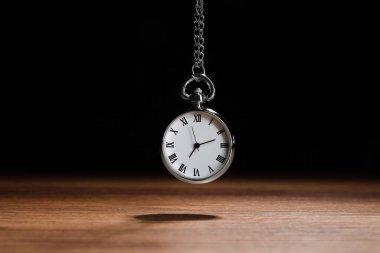 Beautiful vintage pocket watch with silver chain on black background above wooden table. Hypnosis session