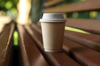 Cardboard takeaway coffee cup with lid on wooden bench outdoors, space for text