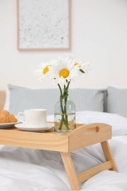 Bouquet of beautiful daisy flowers and breakfast on wooden tray in bedroom