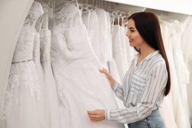 Genç bir kadın gelinliği kuaförde seçiyor.