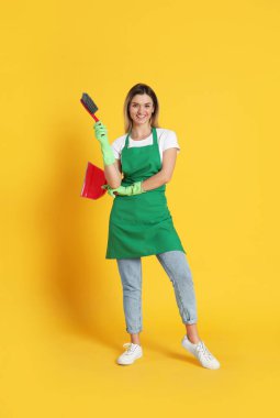 Turuncu arka planda süpürgesi ve faraşı olan genç bir kadın.