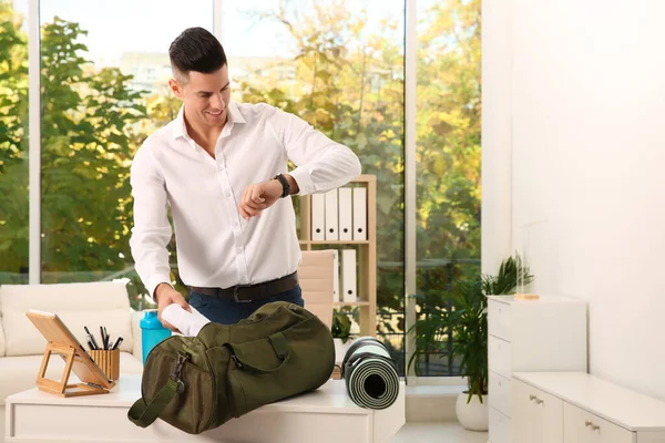 Businessman packing sports stuff for training into bag in office