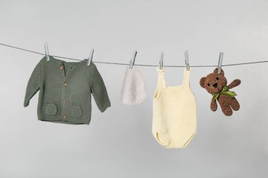Different baby clothes and toy drying on laundry line against light background