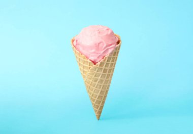Açık mavi arka planda waffle külahında leziz pembe dondurma.