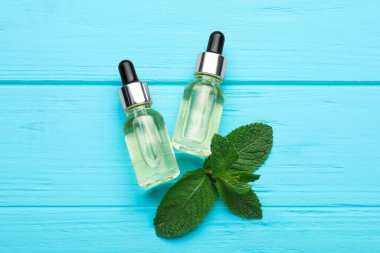 Bottles of essential oil and mint on turquoise wooden table, flat lay