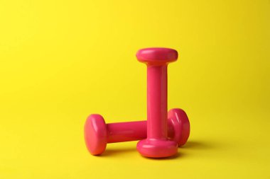 Two stylish pink dumbbells on yellow background