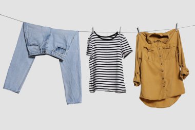 Different clothes drying on laundry line against light background