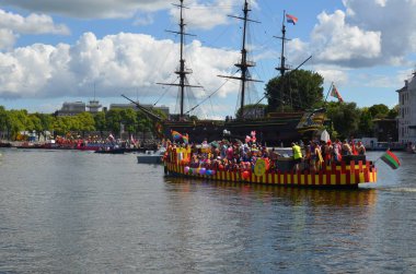 AMSTERDAM, NETHERLANDS - AUGUST 06, 2022: Boats with people holding LGBT pride flags at parade on river