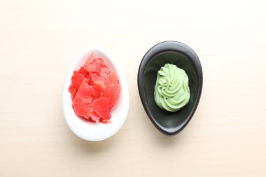 Bowls with swirl of wasabi paste and pickled ginger on white table, flat lay
