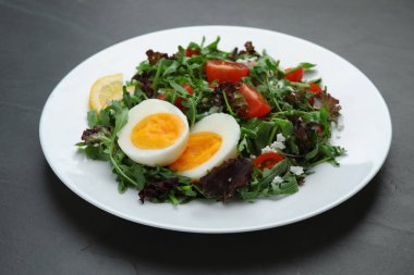 Delicious salad with boiled egg, arugula and tomatoes on black table, closeup