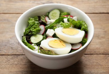 Haşlanmış yumurtalı lezzetli salata, ahşap masada peynir ve sebzeler, yakın plan.