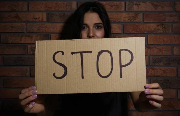 Abused young woman with sign STOP near brick wall. Domestic violence concept