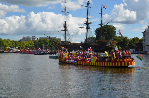 AMSTERDAM, NETHERLANDS - AUGUST 06, 2022: Boats with people holding LGBT pride flags at parade on river
