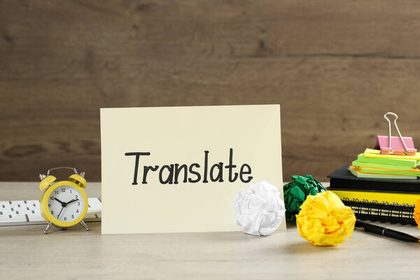 Card with word Translate, alarm clock, paper balls, keyboard and notebooks on wooden table