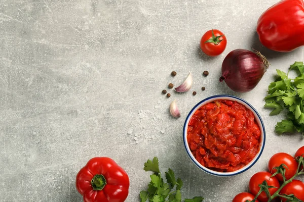 Delicious lecho in bowl and fresh ingredients on light grey table, flat lay. Space for text